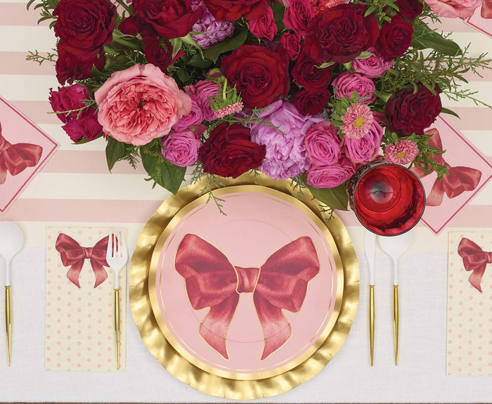Create a charming birthday tablescape with Sophistiplate’s Pink Bows Dinner Plates (8pk)—each plate from the Pink Bows Collection features an elegant pink design with a red bow, perfectly complemented by a gold charger, polka dot napkin, white utensils, a red glass, and a vibrant centerpiece of red and pink flowers atop a striped tablecloth for stylish party tableware.