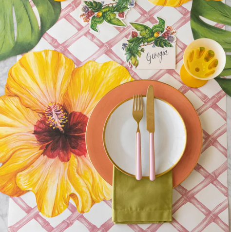 A table setting with a large yellow hibiscus placemat, white plate on a terracotta charger, pink-handled cutlery, olive green napkin, yellow cup, and a Georgia card with florals atop the Hester & Cook Pink Lattice Runner (20x25").