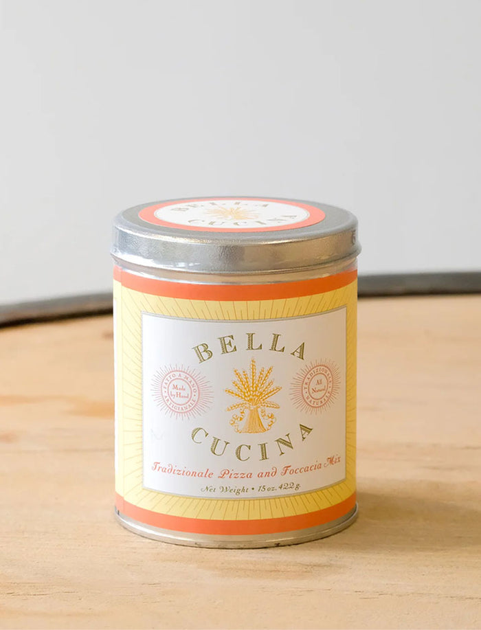 A metal canister labeled Bella Cucina Traditional Pizza and Focaccia Mix sits on wood—perfect to pair with Maple’s Personalized Pizza Peel Gift Set for the ultimate pizza night. The cream and orange label features decorative text.