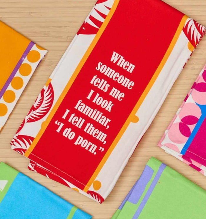 The Porn Dish Towel by Drinks On Me features a funny quote and stands out among colorful patterned cloths, making it a perfect novelty housewarming gift for those who love to laugh.