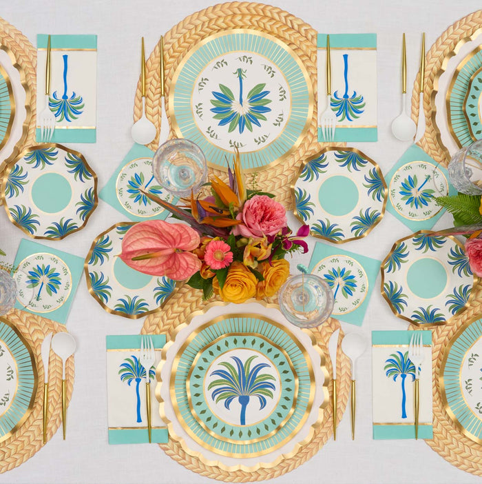 A tropical table for six features Sophistiplate Preppy Palm Salad Plates, gold utensils, turquoise accents, woven placemats for texture, and a vibrant pink and orange floral centerpiece.
