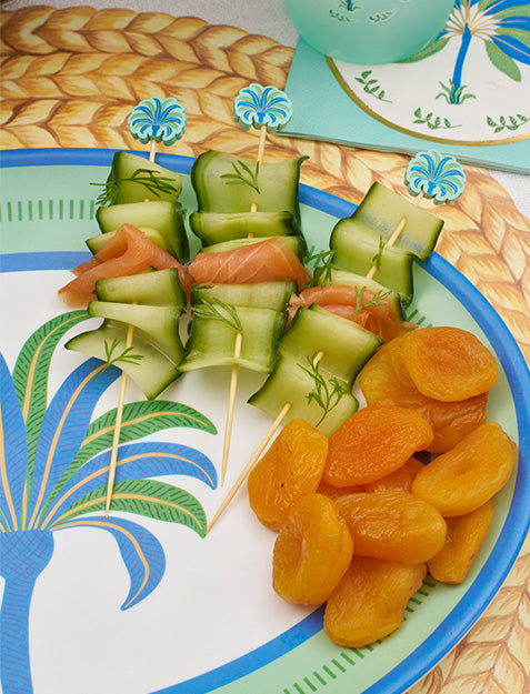 Cucumber and smoked salmon skewers with dill, garnished with blue picks and dried apricots, are artfully presented on the Sophistiplate Preppy Palm Melamine Serving Platter with a coordinating placemat and napkin.