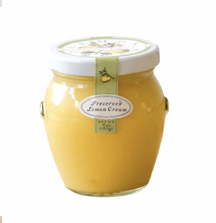 A glass jar of Bella Cucina Preserved Lemon Cream, a citrus spread with preserved lemons, is sealed with a white lid, decorated with a green ribbon and oval label, and displayed on a white background.