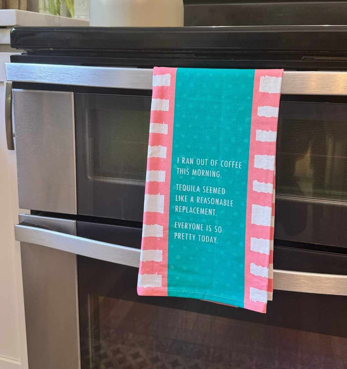 The Drinks On Me "Ran Out of Coffee Dish Towel" hangs on an oven handle, making a fun housewarming gift. It reads: I ran out of coffee this morning. Tequila seemed like a reasonable replacement. Everyone is so pretty today.