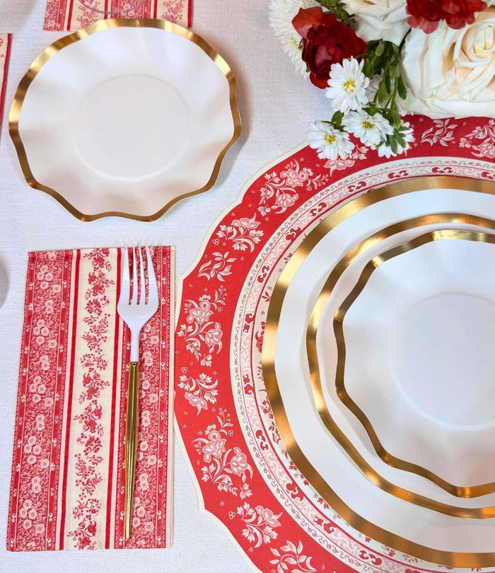 The Sophistiplate Red Burleigh Table Setting features designer disposable plates with gold edges on red and white floral placemats, a fork on a striped napkin, and coordinated flowers for an elegant tablescape-in-a-box.