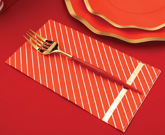 A Sophistiplate Red & Gold Bella Plastic Fork from the 24pc, service for 8 set rests on a striped red napkin, with matching red plates featuring gold trim in the background, all arranged on a bold red surface.