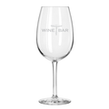 A clear, empty Maple Reserve Wine Glass | Wine Bar | 19.75oz stands upright on a white background, featuring a gray laser-engraved WINE BAR and corkscrew logo on the bowl.