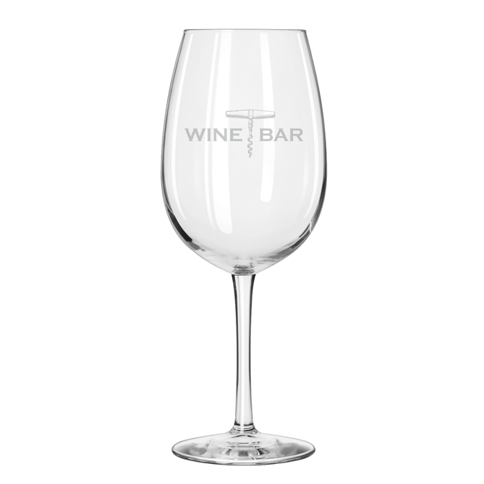 A clear, empty Maple Reserve Wine Glass | Wine Bar | 19.75oz stands upright on a white background, featuring a gray laser-engraved WINE BAR and corkscrew logo on the bowl.