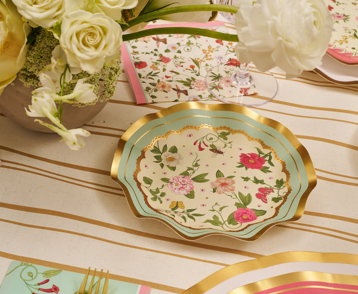 The Rococo Table Setting by Sophistiplate LLC features designer plates with gold and turquoise edges and floral designs, displayed on a striped tablecloth with matching floral napkins—ideal for your next party-in-a-box celebration.