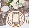 The Royal Peacock Table Setting - Brown & White by Sophistiplate features designer disposable plates, a floral menu, white and gold cutlery, and a centerpiece with white and pale pink roses on a brown floral tablecloth.