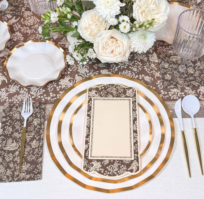 The Royal Peacock Table Setting - Brown & White by Sophistiplate features designer disposable plates, a floral menu, white and gold cutlery, and a centerpiece with white and pale pink roses on a brown floral tablecloth.