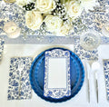 The Royal Peacock Table Setting - French Blue by Sophistiplate features blue and white floral napkins, designer plates, a menu card, silver cutlery, crystal glassware, white roses and baby's breath centerpiece, and a lit candle on a matching runner.