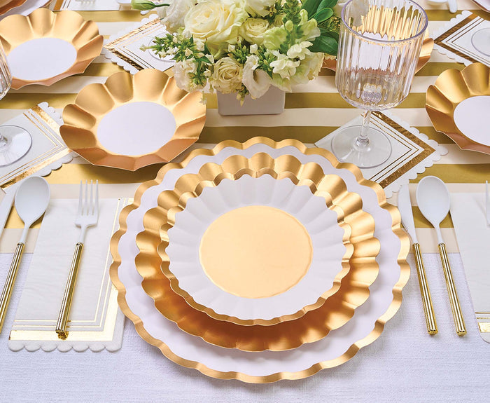 Sophistiplate Salad Plate Gold & White (8/pkg) brings elegance to your table, paired with gold utensils, a wine glass, white napkins, and a gold-striped tablecloth. A floral centerpiece with white flowers completes the festive holiday look.