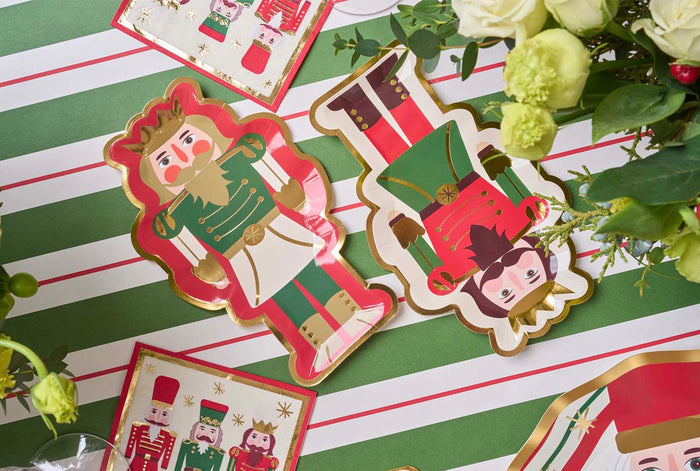 Create a festive table with Sophistiplate's Salad Plate Nutcracker Christmas Assorted (8/pkg), set on a white and green striped tablecloth and surrounded by matching flowers.