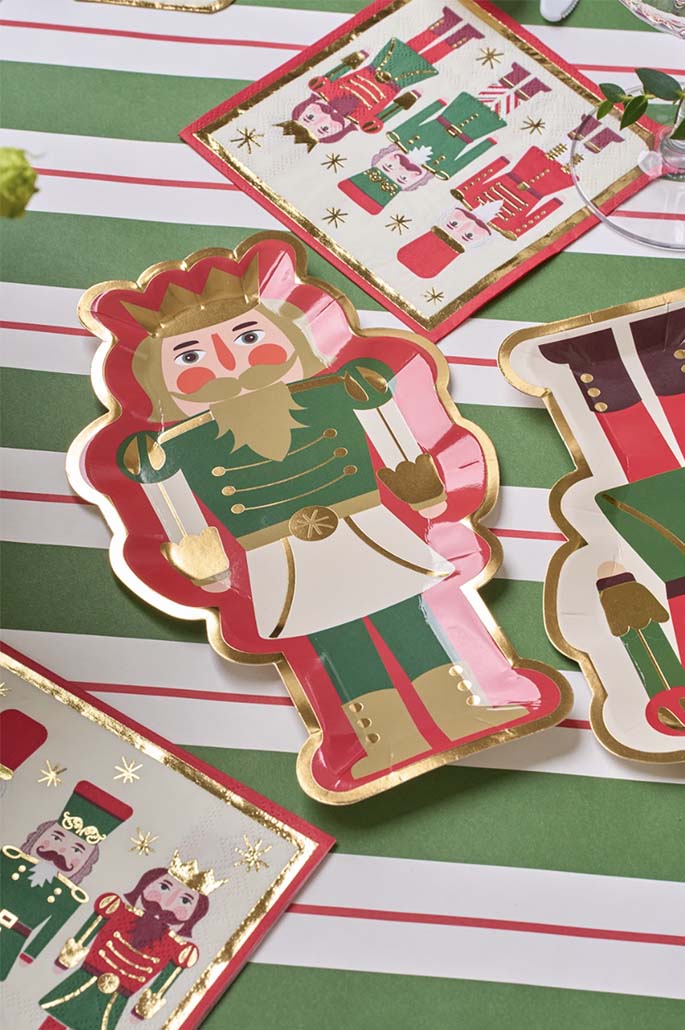 Create a festive table with Sophistiplate's Salad Plate Nutcracker Christmas Assorted 8-pack, featuring colorful nutcracker designs, paired with napkins on a red, white, and green striped tablecloth.