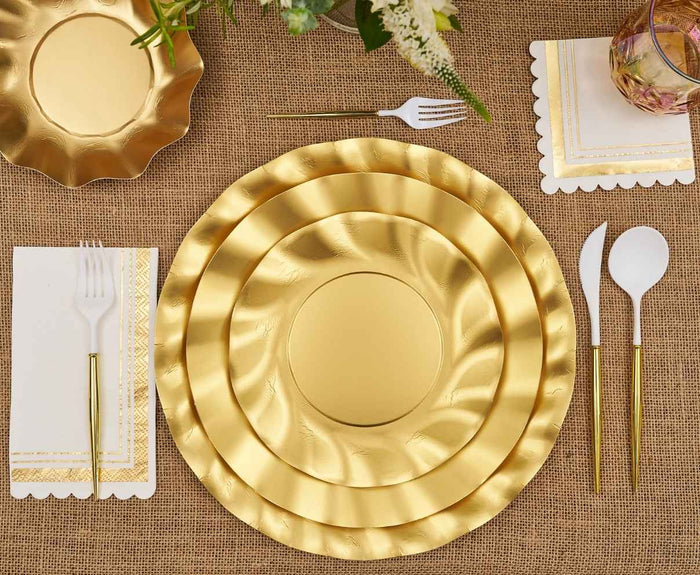 The Satin Gold Table Setting by Sophistiplate LLC includes three nested designer plates, white cutlery with gold handles, scalloped napkins, and a glass on burlap—decorative flowers add flair. Perfect for a chic party-in-a-box.