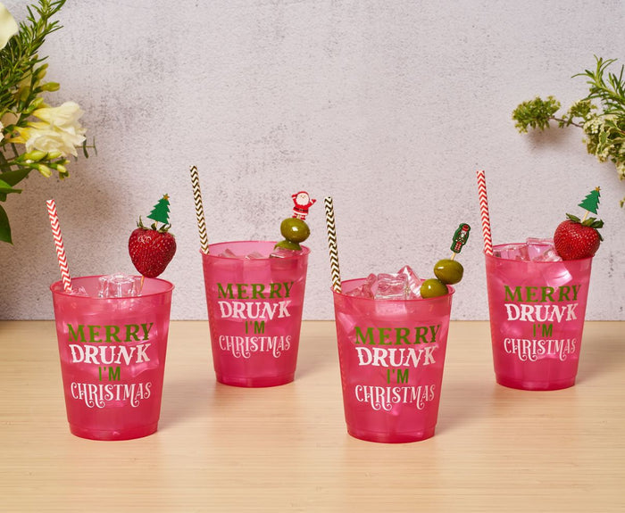 Four pink cups with "Merry Drunk I'm Christmas" text, filled with ice and decorated using Scarlet Chevron Paper Cocktail Straws by Simply Serv'd, strawberries, olives, and festive toppers—perfect for a fun holiday hostess gift.