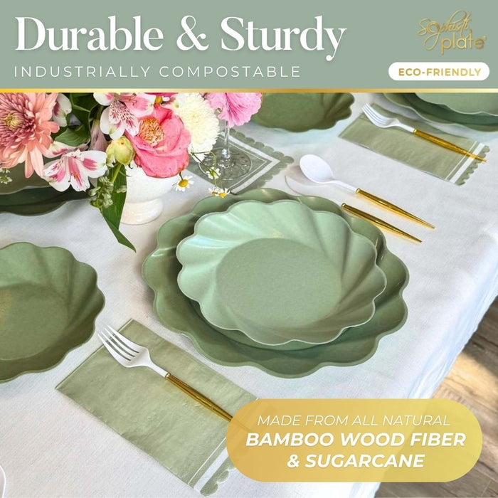 A Sophistiplate LLC Eco-friendly Table Setting- Sage features green, scalloped-edge compostable plates made from bamboo wood fiber and sugarcane, gold-handled cutlery, and white utensils arranged around a floral centerpiece.
