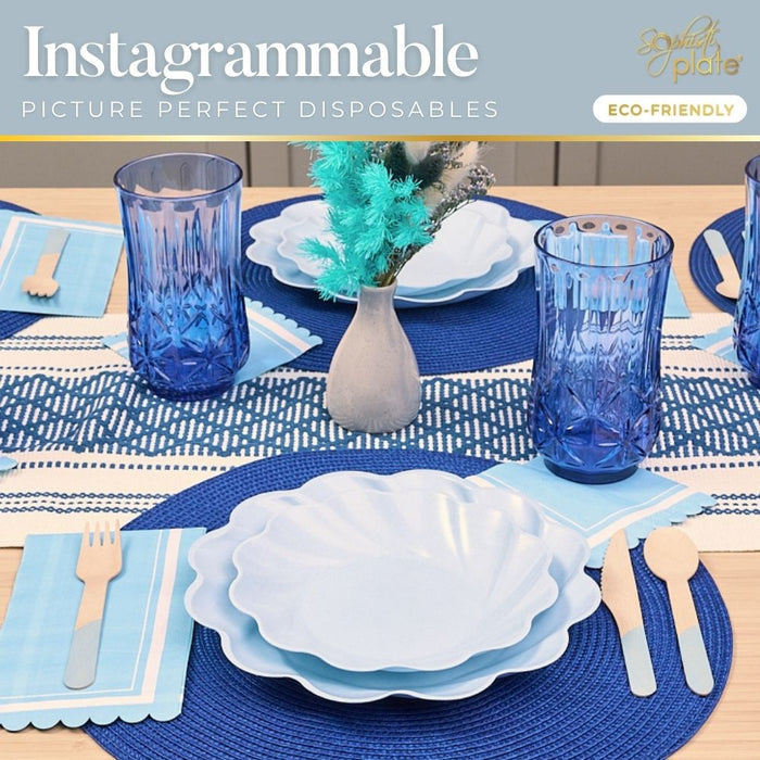 Create a stylish table with the Sophistiplate Eco-Friendly Table Setting—Sky Blue, featuring layered compostable plates, blue tumblers, wooden cutlery on blue napkins, and blue and white flowers atop a woven placemat and decorative runner.