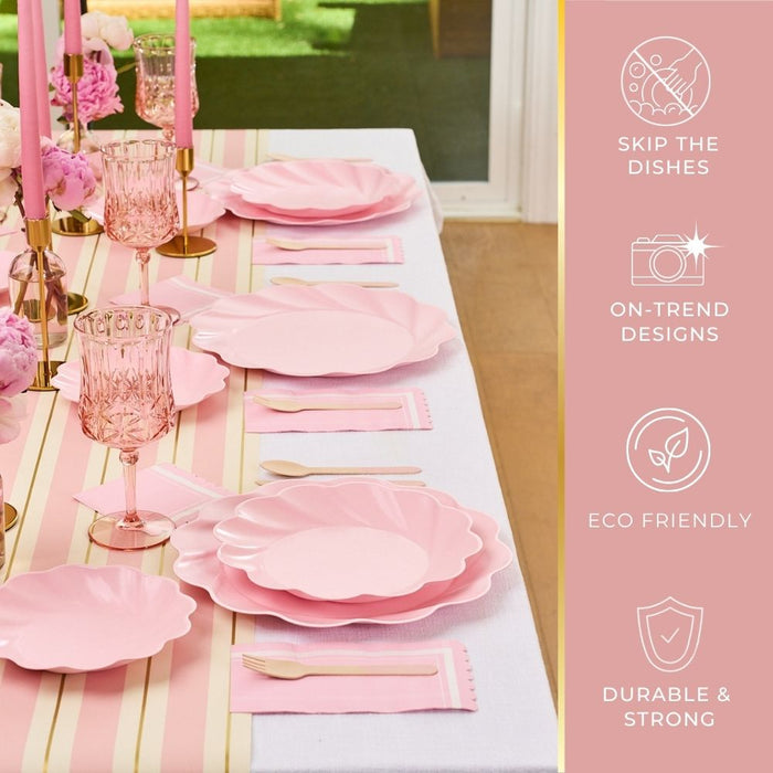 The Sophistiplate Eco-Friendly Table Setting- Blush features pink scalloped compostable party plates, pink glassware, gold flatware, and blush candles on a white cloth with pink and gold stripes—disposable, durable, and chic.
