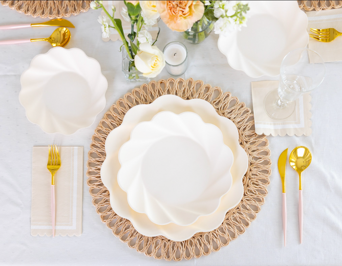 Elegant table setting featuring Sophistiplate LLC’s Eco Cream & Blush Cutlery Bundle on a woven placemat, paired with eco-friendly plates, white napkins, glassware, and small white and yellow floral arrangements atop a light tablecloth.