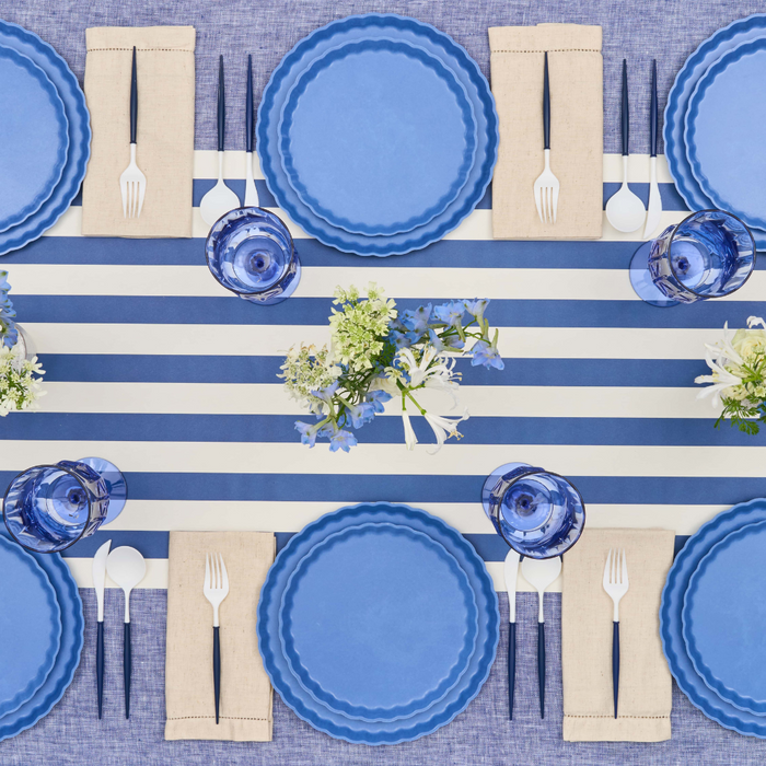 Aerial view of a table for six set with Sophistiplate Simply Eco Salad Plate-French Blue, blue glasses, beige napkins, white cutlery, small floral centerpieces, and a blue and white striped table runner.
