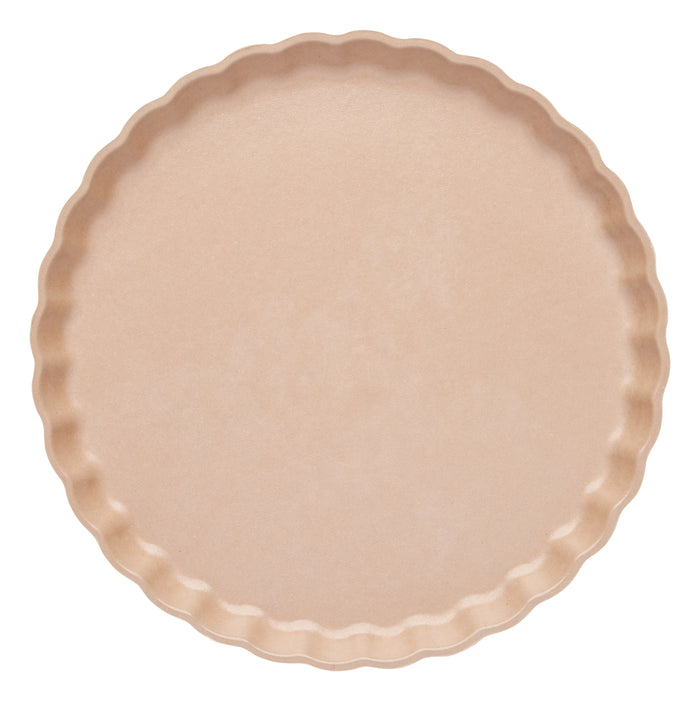 An unfilled, uncooked round beige tart crust with fluted edges sits atop a Sophistiplate Simply Eco Salad Plate- Sand/8pkg, shown from above against a white background—an eco-friendly tableware option for sustainable baking.