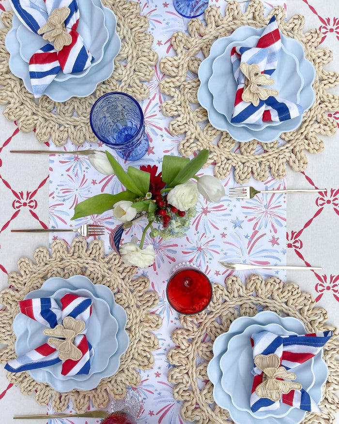 Create a festive table with Sophistiplate's Eco-Friendly Table Setting in Sky Blue, paired with red, white, and blue napkins, woven placemats, colored glasses, gold utensils, and a vase of white and red flowers.