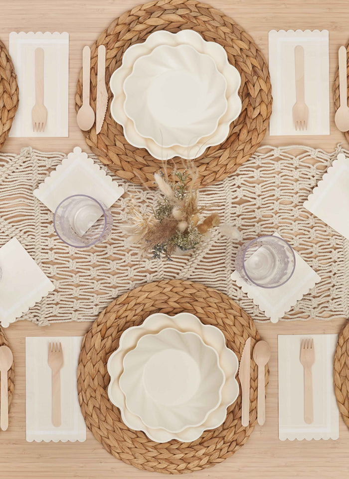 Experience the Stunning Seder Table Setting by Sophistiplate featuring woven placemats, designer disposable plates, wooden cutlery, clear glasses, white napkins, a macrame runner, and a dried floral centerpiece.