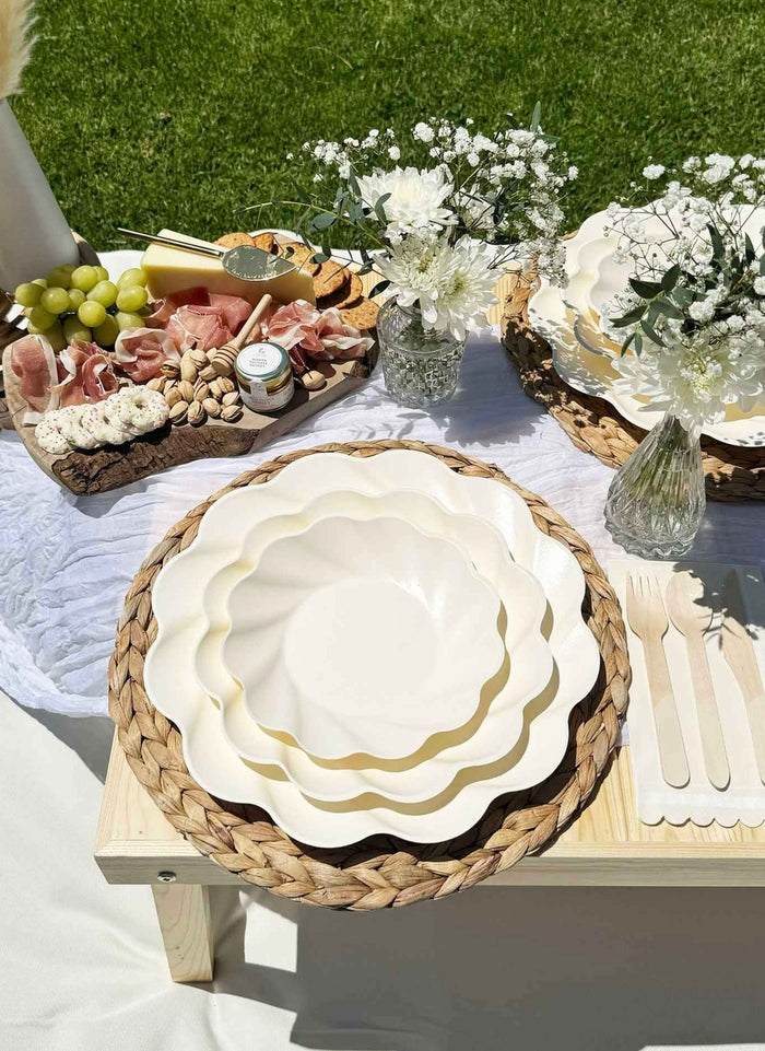 Enjoy an elegant picnic with the Sophistiplate Stunning Seder Table Setting, featuring stacked designer disposable plates, wooden cutlery, vases with white flowers, and a charcuterie board—your complete tablescape-in-a-box.