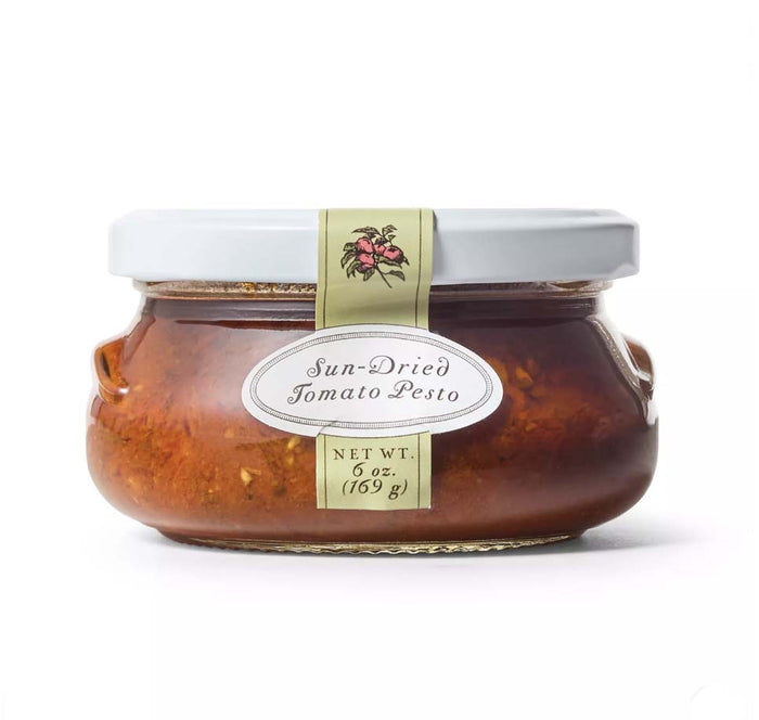 A glass jar of Bella Cucina Sun-dried Tomato Pesto, made with Parmesan and extra virgin olive oil, sealed with a white lid and labeled Sun-dried Tomato Pesto, Net Wt. 6 oz. (169 g).