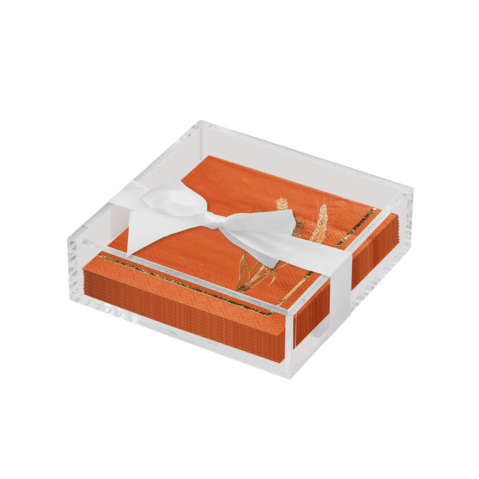 The Sophistiplate Thanksgiving Cocktail Napkin with Napkin Tray features orange napkins with a gold botanical design in a clear acrylic square holder, tied with a white satin ribbon—ideal for modern tables.