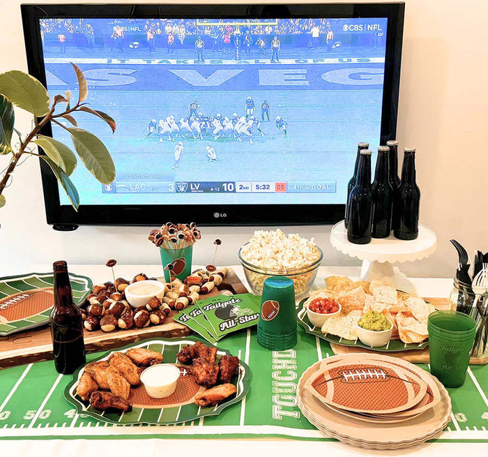 The Superbowl Set by Sophistiplate includes designer disposable plates and a green table cover with white markings, perfect for serving wings, sliders, chips, dips, popcorn, and drinks while watching the big game.