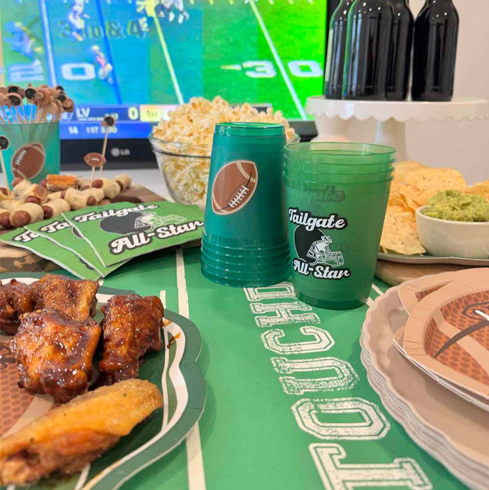 The Superbowl Set by Sophistiplate features football-themed wings, chips, popcorn, snacks, designer disposable plates, and green cups—everything you need for a party-in-a-box while you enjoy the game on TV.