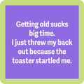 A purple square with a light green border reads: Getting old sucks big time. I just threw my back out because the toaster startled me. The Coaster Bundle: Birthday by Drinks On Me is a hilarious gift for friends who love to laugh.