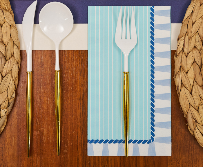 The Sophistiplate Tidal Wave Table Setting features white cutlery with gold handles and a blue striped napkin on woven placemats—perfect for stylish coastal party decor.