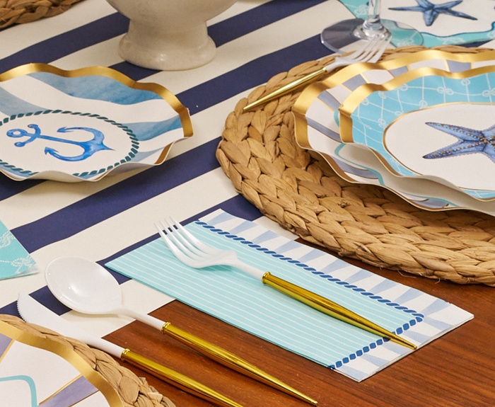 The Sophistiplate Tidal Wave Table Setting features anchor and starfish plates, gold cutlery, woven placemats, striped napkins, and a white fork and spoon—everything you need for chic coastal party decor in one box.