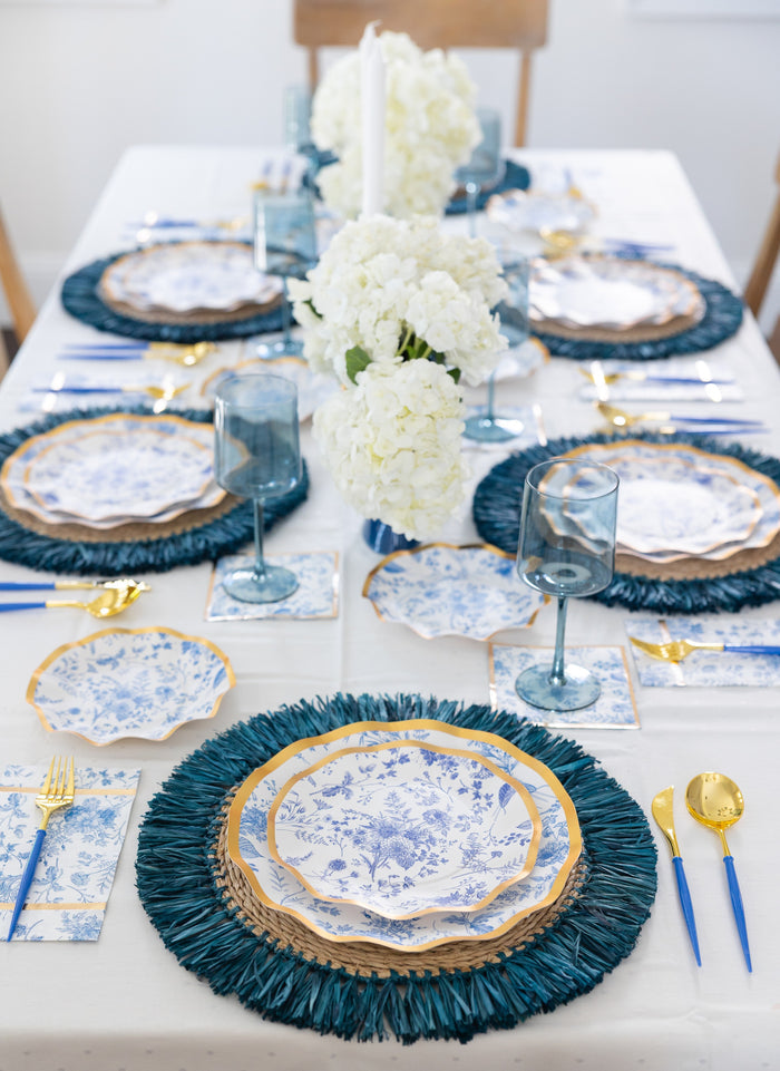 For a stylish holiday party, set your table with Sophistiplate’s Timeless Dinner Plates (8pk), featuring a classic blue and white floral design with a metallic gold rim. Pair these elegant plates with gold utensils, blue glasses, and white hydrangea centerpieces, arranged neatly on a crisp white tablecloth with coordinating blue placemats.