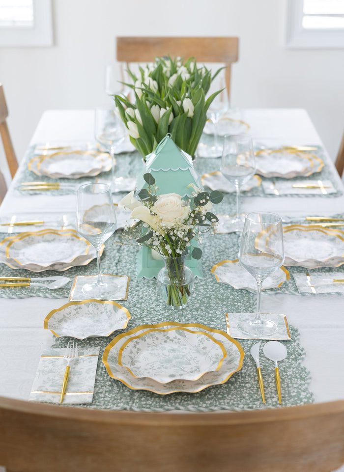 A formal table setting with white tulips, floral centerpiece, and plates with gold rims on a green runner includes Sophistiplate Timeless Sage Appetizer/Dessert Bowls (8pk) for added charm.