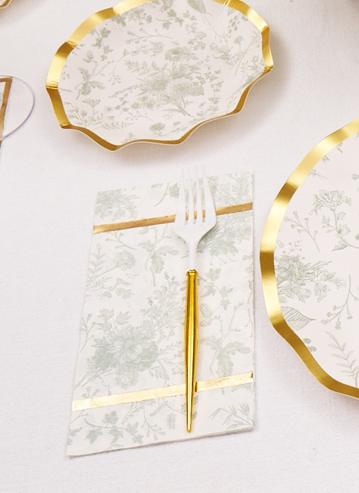 A Sophistiplate Timeless Sage Guest Towel from the 20pk rests on an elegant table, paired with matching plates and gold-accented cutlery.