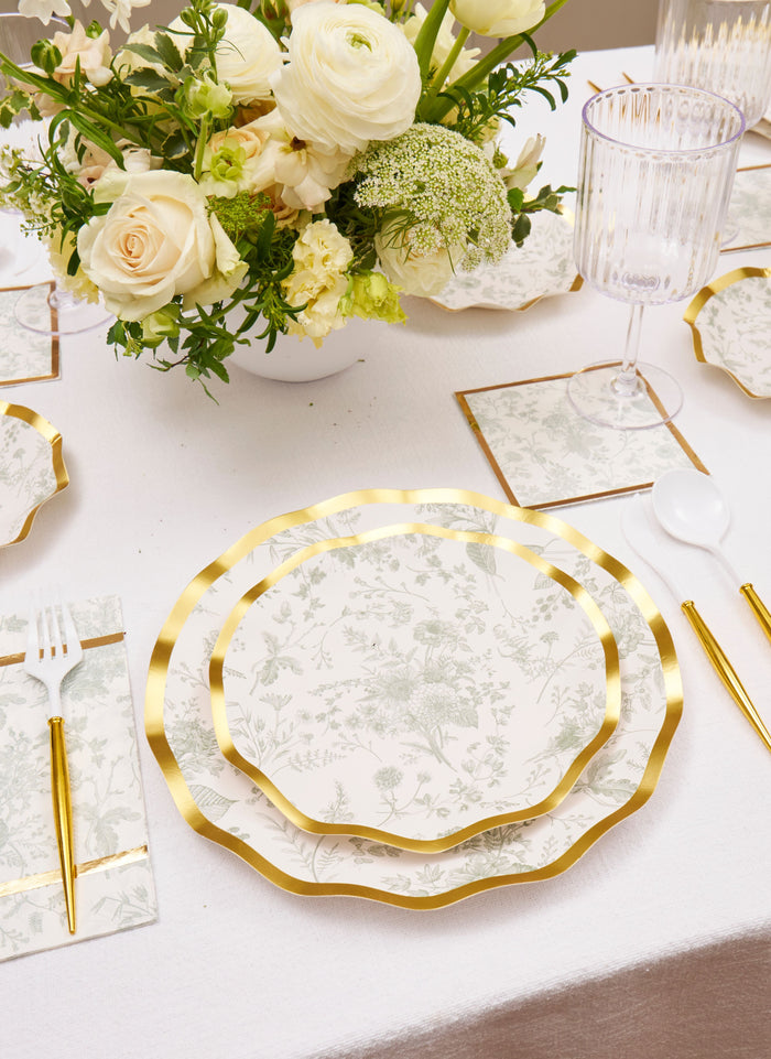 Elegant table setting featuring Sophistiplate’s Timeless Sage Salad Plates (8pk), gold-edged utensils, clear ribbed glasses, and a centerpiece of white and cream flowers on a white tablecloth.