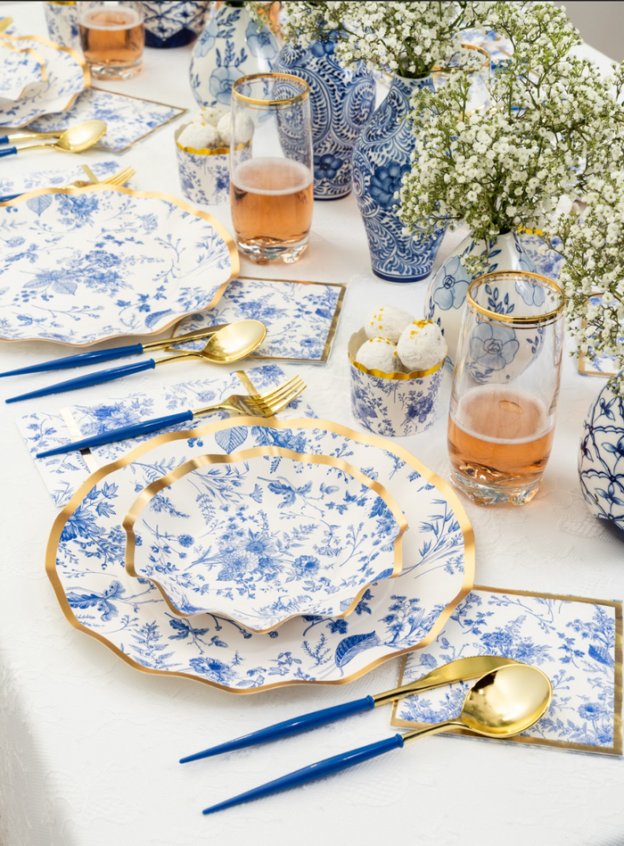 The table boasts an elegant setting with blue and white floral plates, gold-rimmed glasses, gold and blue cutlery, and floral vases filled with baby’s breath flowers. Completing the sophisticated, coordinated design are Sophistiplate Timeless Guest Towels (20pk), whose elegant style perfectly complements the refined atmosphere.