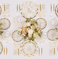 Experience the Timeless Table Setting: Sand by Sophistiplate, featuring gold-rimmed designer paper plates, floral-patterned napkins, elegant gold cutlery, clear glasses, and a stunning centerpiece of white and blush flowers beautifully arranged on a crisp white tablecloth.