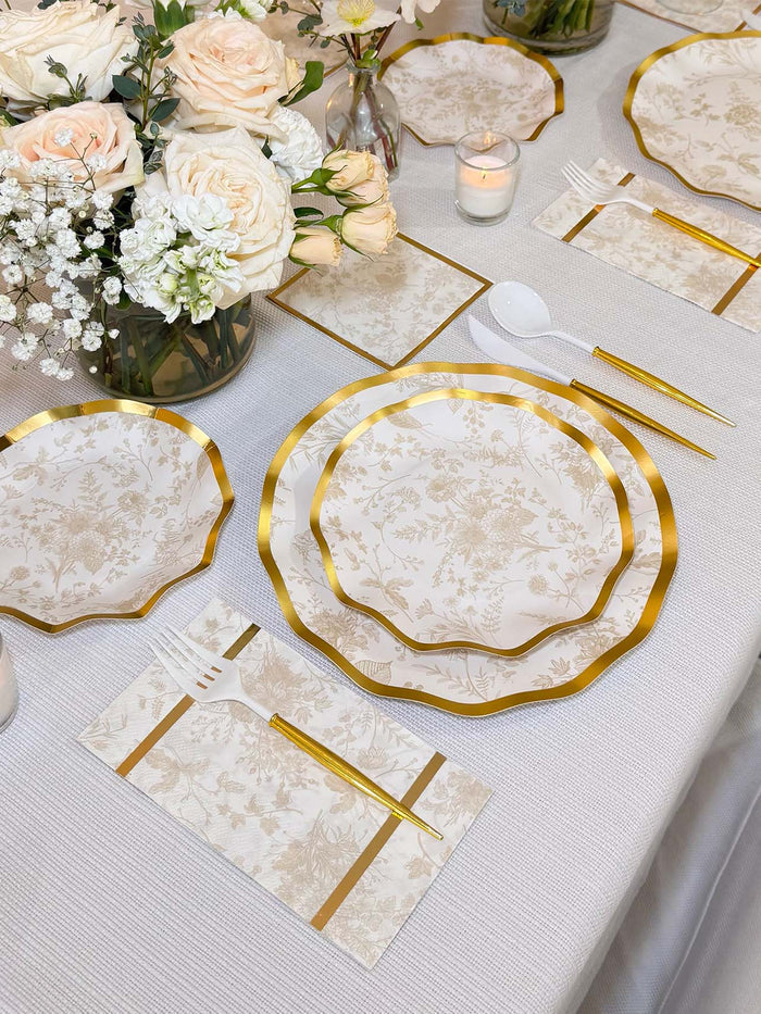 Create an elegant tablescape with Sophistiplate’s Timeless Table Setting: Sand, featuring designer disposable plates, matching cutlery, floral napkins, and a centerpiece of white and blush roses with greenery on a white tablecloth.