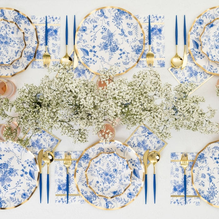 Create a luxe party-in-a-box with the Timeless Table Setting by Sophistiplate—featuring designer blue and white floral plates, gold utensils, blue-handled cutlery, and baby's breath centerpiece on a white tablecloth.