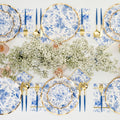 Create a luxe party-in-a-box with the Timeless Table Setting by Sophistiplate—featuring designer blue and white floral plates, gold utensils, blue-handled cutlery, and baby's breath centerpiece on a white tablecloth.