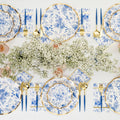 The Timeless Table Setting features blue and white floral heavy-duty paper plates, gold utensils, blue-handled cutlery, pink drinks in glasses, and a white baby's breath centerpiece—everything for a charming party-in-a-box.