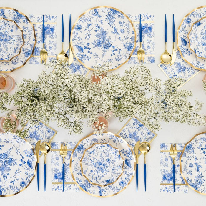 The Timeless Table Setting features blue and white floral heavy-duty paper plates, gold utensils, blue-handled cutlery, pink drinks in glasses, and a white baby's breath centerpiece—everything for a charming party-in-a-box.