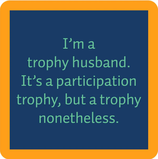 The Drinks On Me Trophy Coaster features a blue square with an orange border and the phrase “I’m a trophy husband. It’s a participation trophy, but a trophy nonetheless”—a fun addition to any bar cart or quirky housewarming gift.