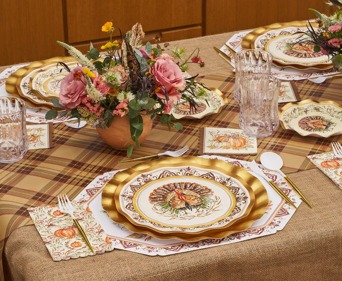 Create a beautiful Thanksgiving tablescape with the Turkey & Gourds Table Setting Bundle by Sophistiplate LLC, featuring a plaid tablecloth, gold-trimmed designer disposable plates adorned with turkeys and gourds, elegant crystal glasses, a floral centerpiece of pink roses, and autumn-themed napkins decorated with pumpkins and leaves.